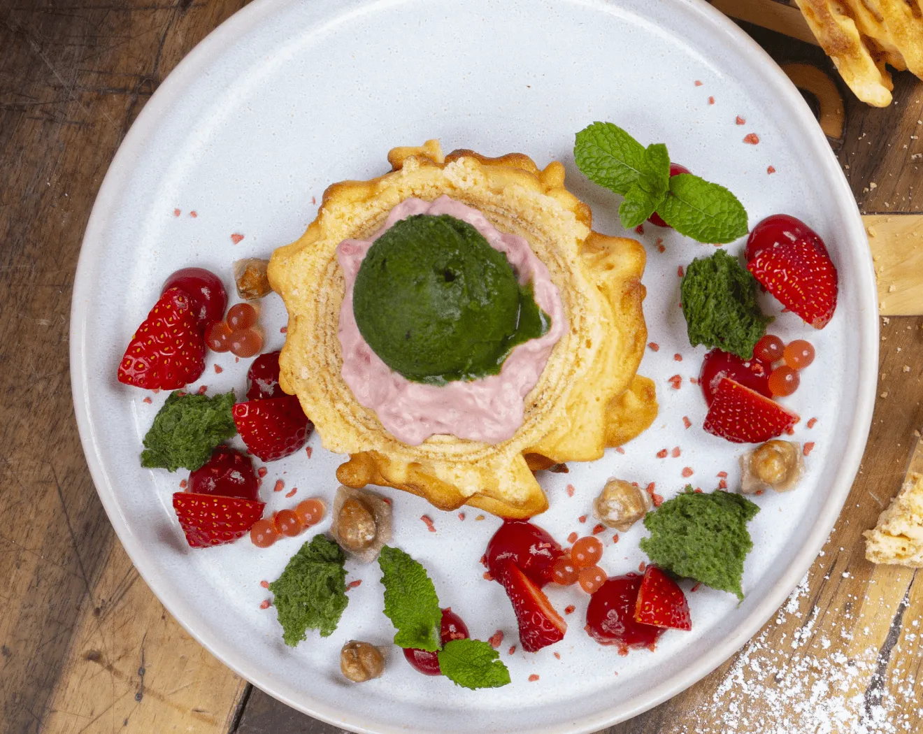 Dessert on a plate with green and pink ice cream, strawberries, and herbs